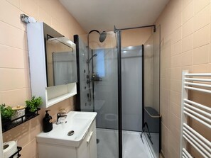 Un baño moderno con cabina de ducha de vidrio, un lavamanos blanco y un espejo sobre él.