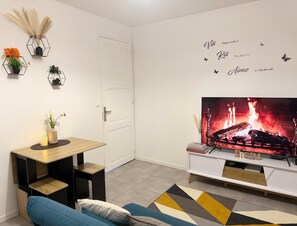 Una sala moderna con una televisión de pantalla plana, una pequeña mesa de comedor, un sofá y decoración en la pared.