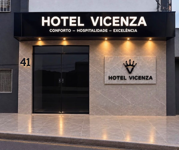 Fachada moderna de un hotel con una entrada destacada, un logotipo con forma de corona y el nombre 'HOTEL VICENZA' exhibido sobre las puertas.