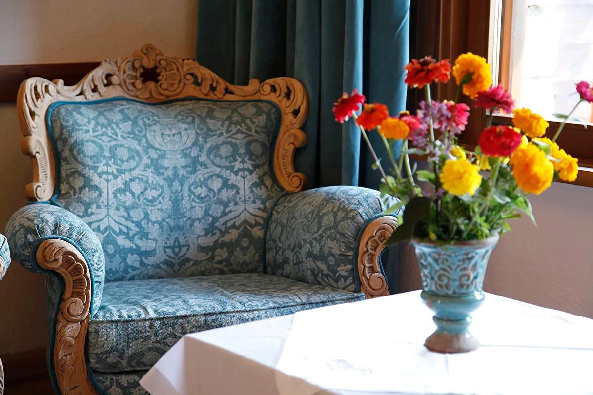 A room with a patterned sofa, a table with a vase of flowers, and a window with curtains.
