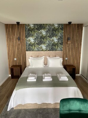 Quarto com uma cama grande, duas mesas de cabeceira, uma cadeira verde e uma parede com ripas de madeira verticais.