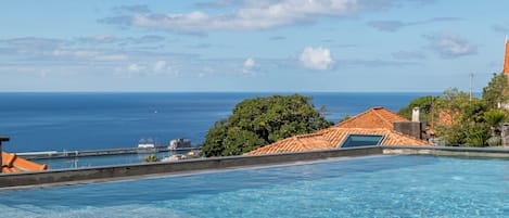 Piscina com vista para o oceano e um porto ao longe.