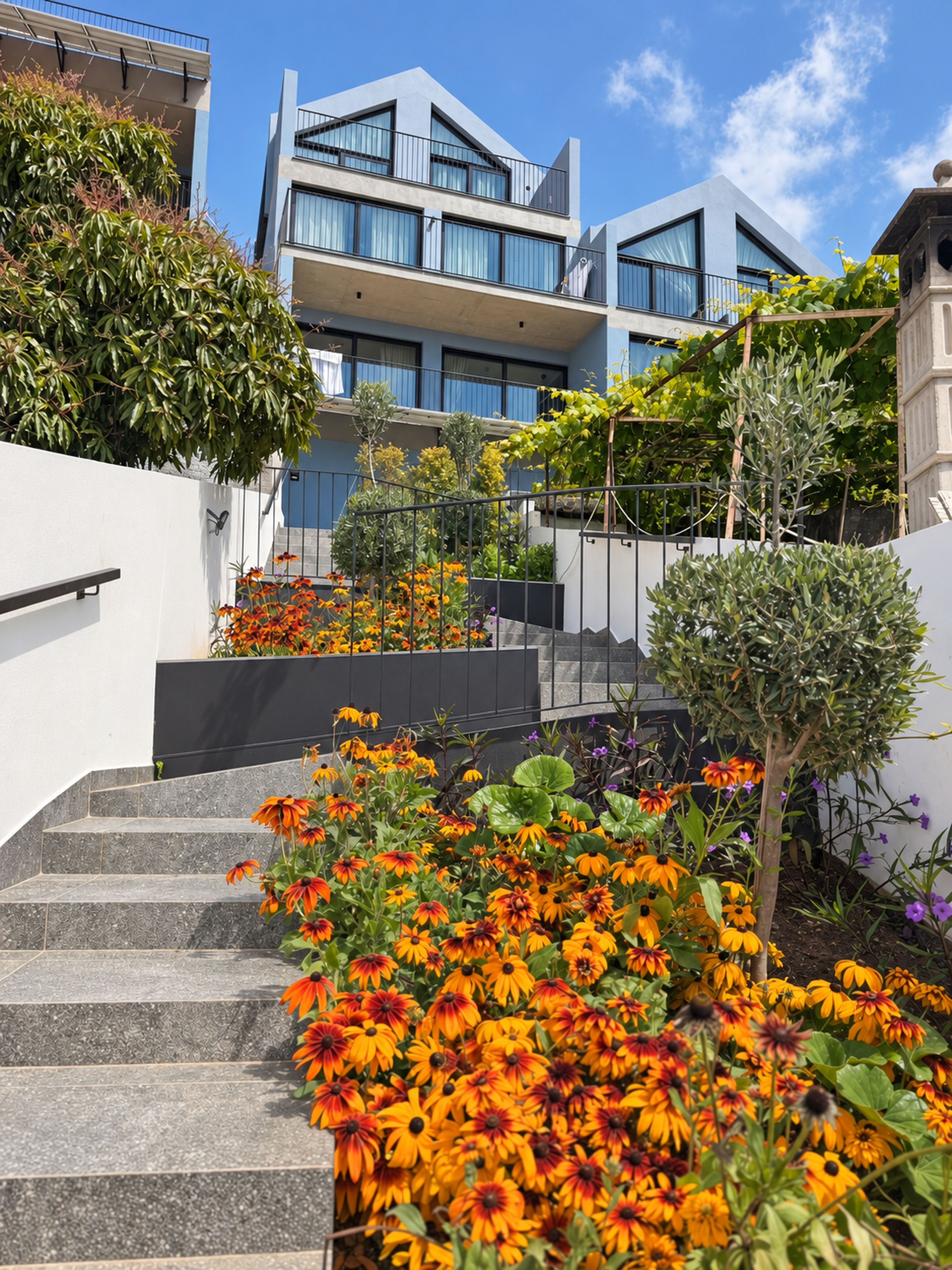 Un edificio moderno con una escalera que lleva a un balcón, rodeado de flores y follaje vibrantes.