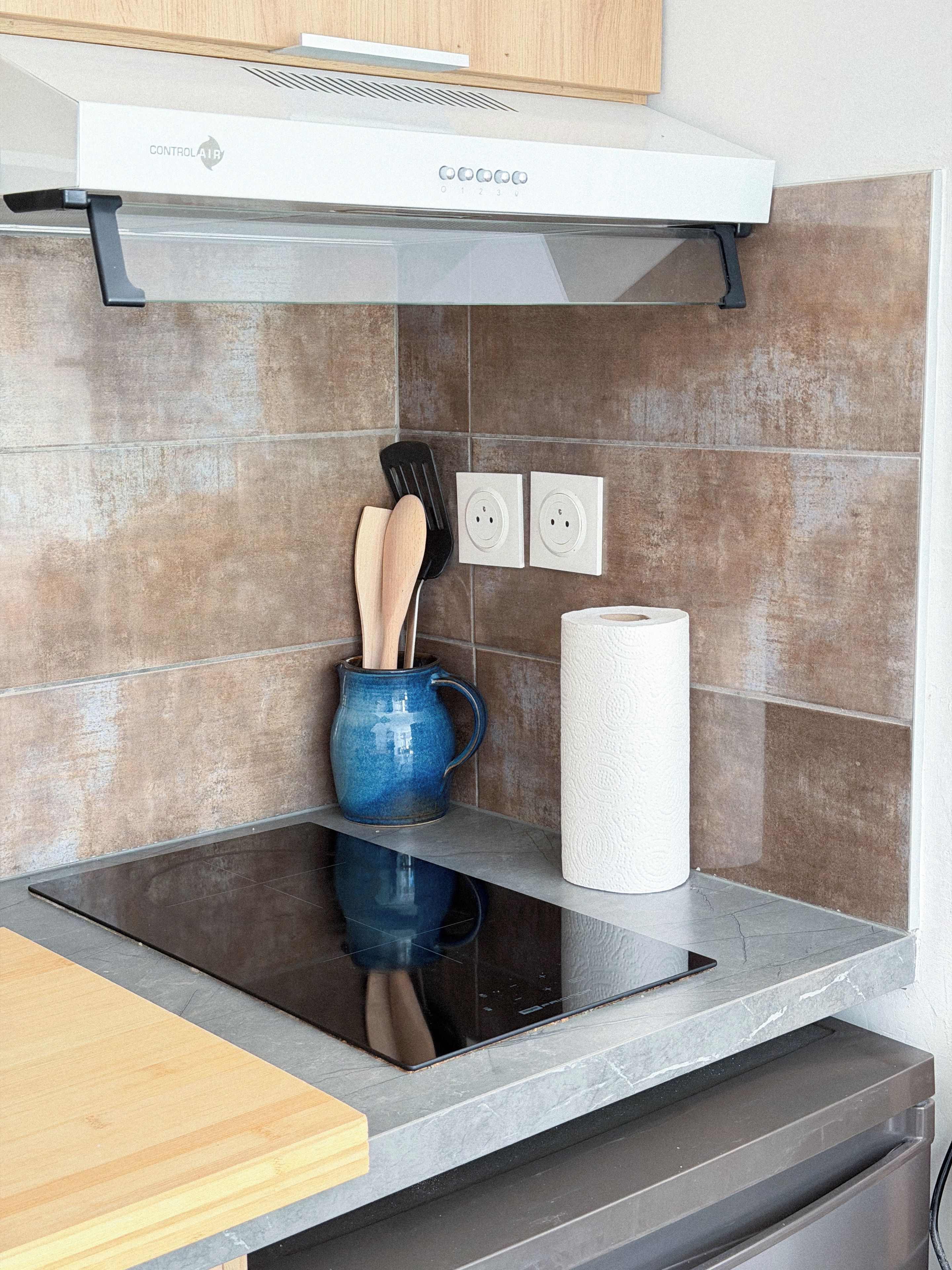 Une cuisine équipée d’une cuisinière intégrée, une tasse bleue, des ustensiles en bois et un rouleau d’essuie-tout.
