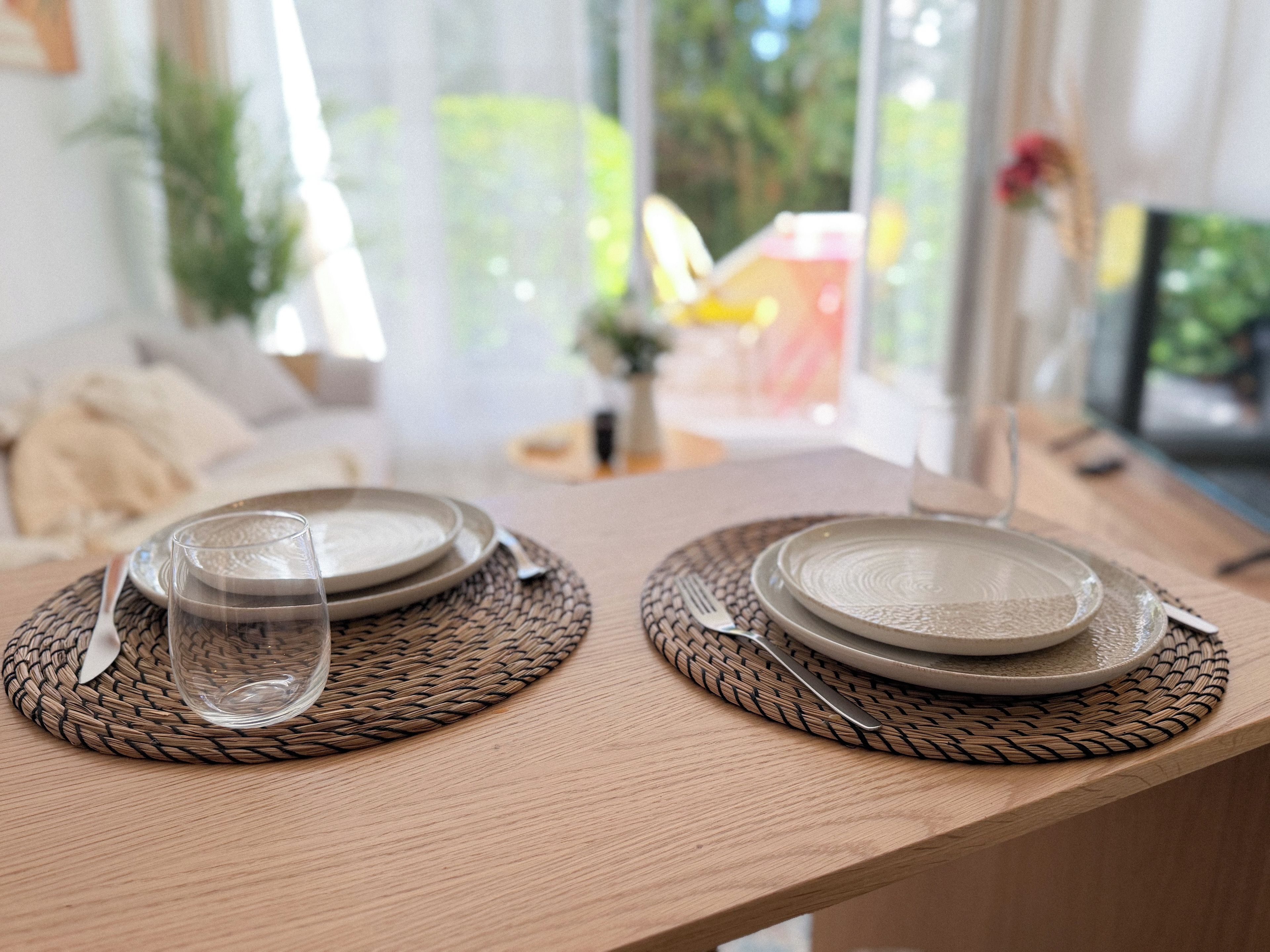 A dining table set with plates, a glass, and cutlery, with a woven placemat.