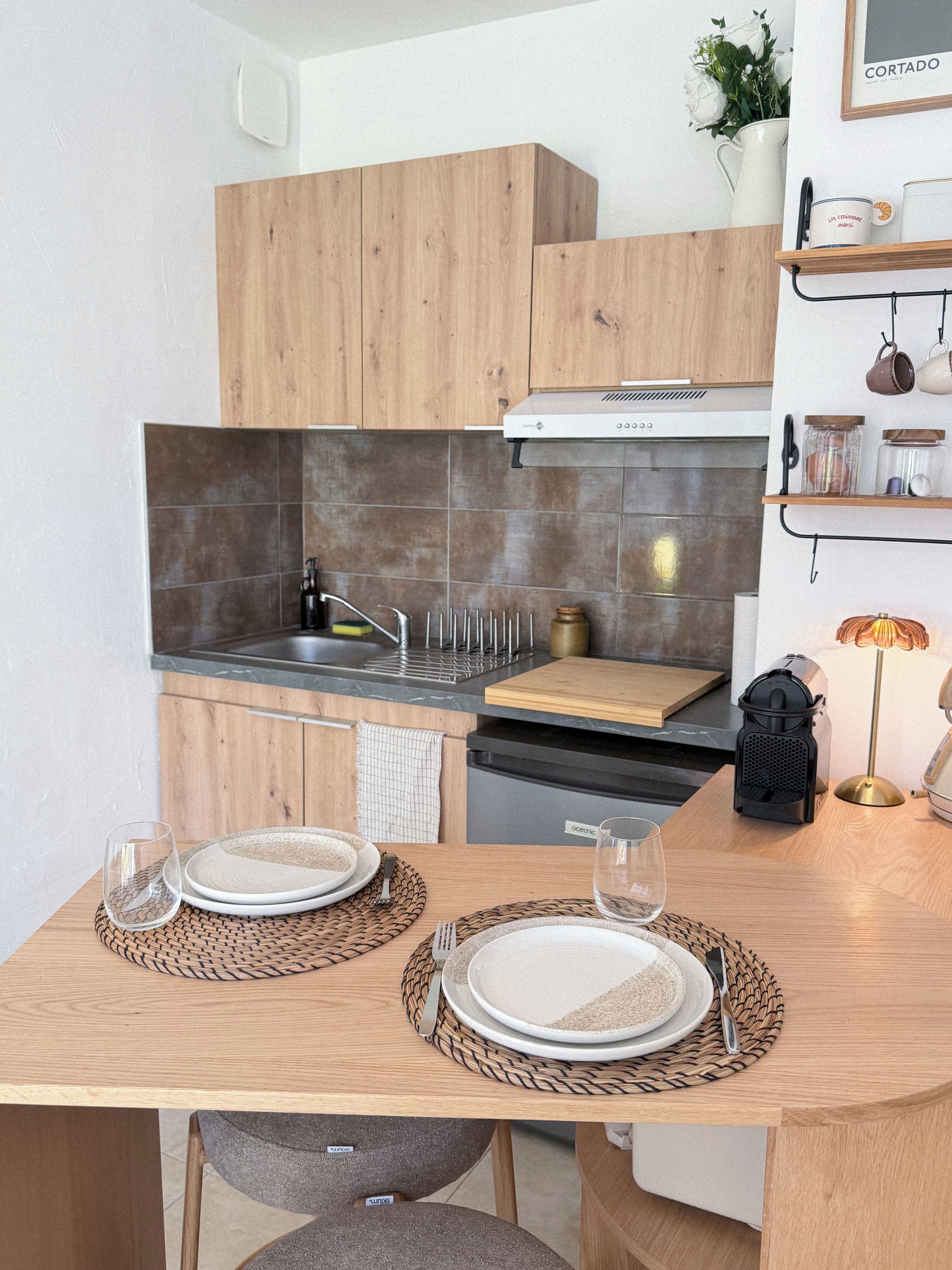 A modern kitchen with wooden cabinets, a stainless steel sink, and a dining table set with plates and cutlery.