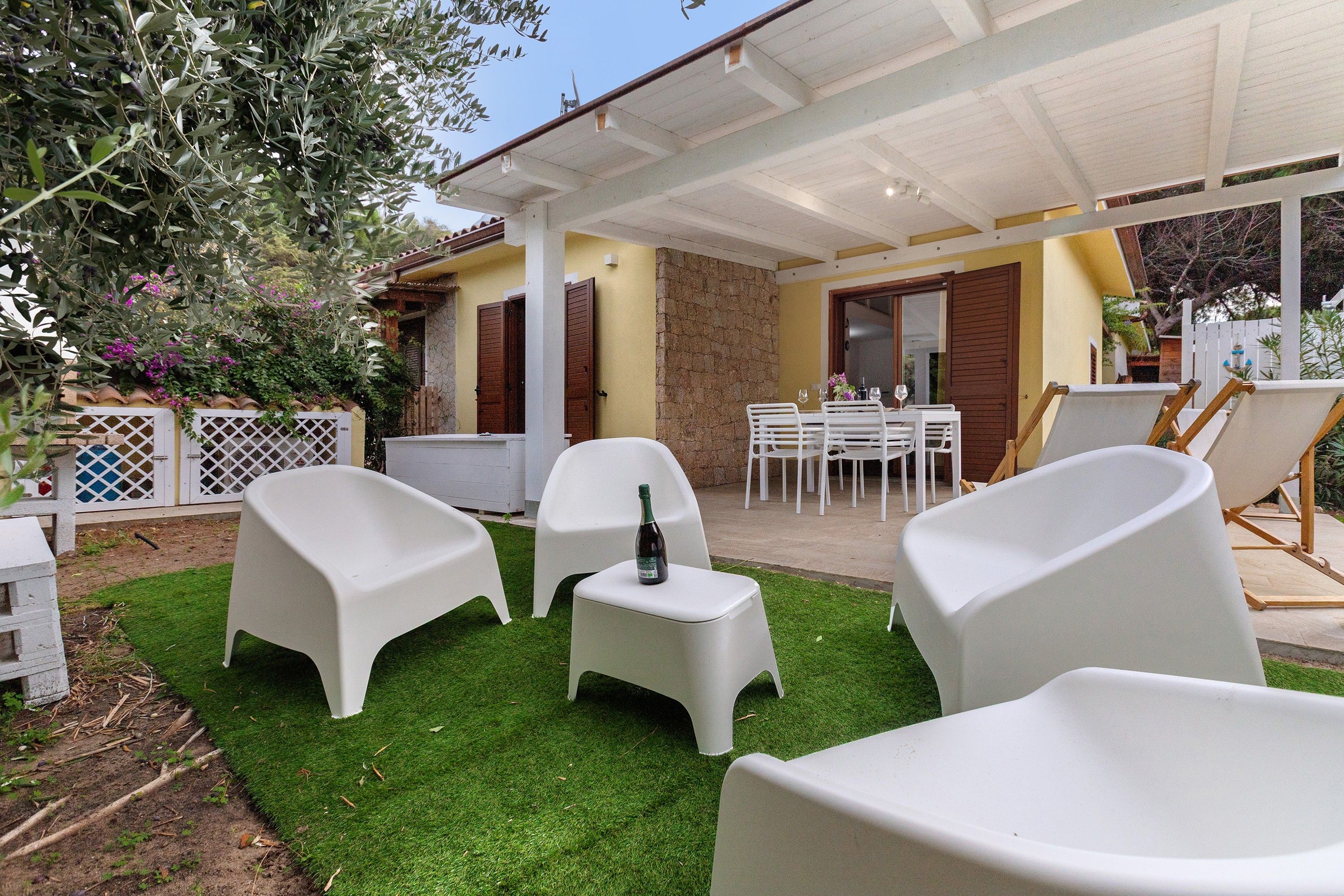 An outdoor patio with white plastic chairs, a small table, and a bottle of wine.