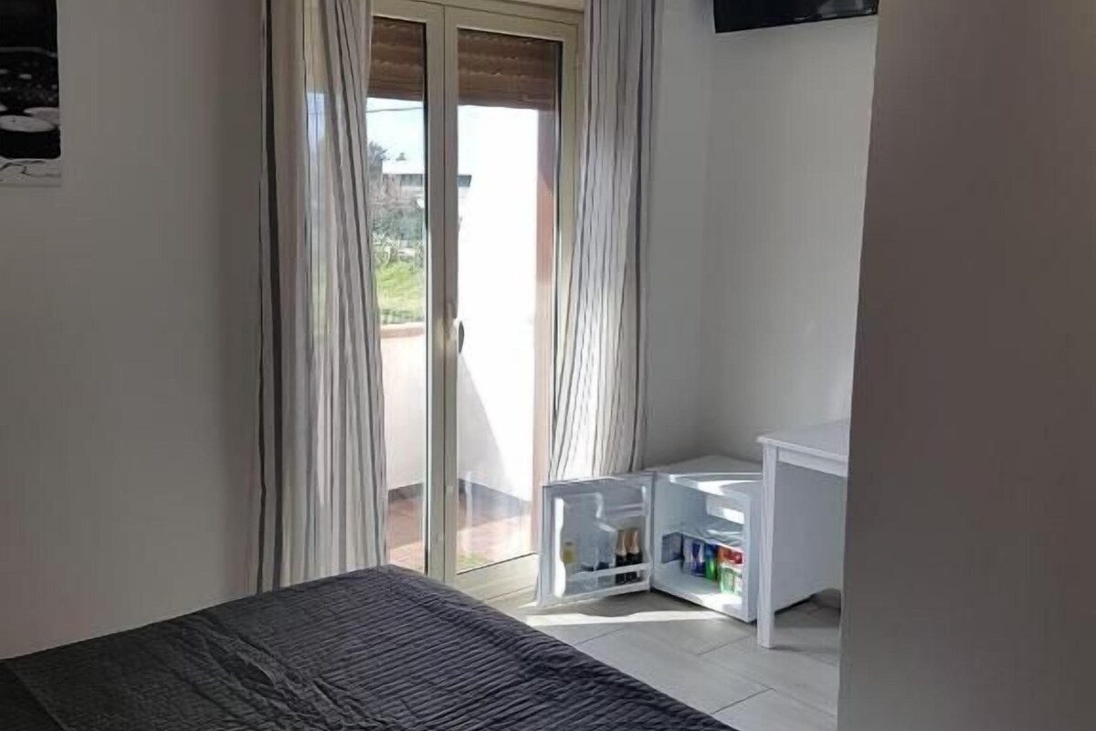 Quarto com cama, escrivaninha e televisão na parede.