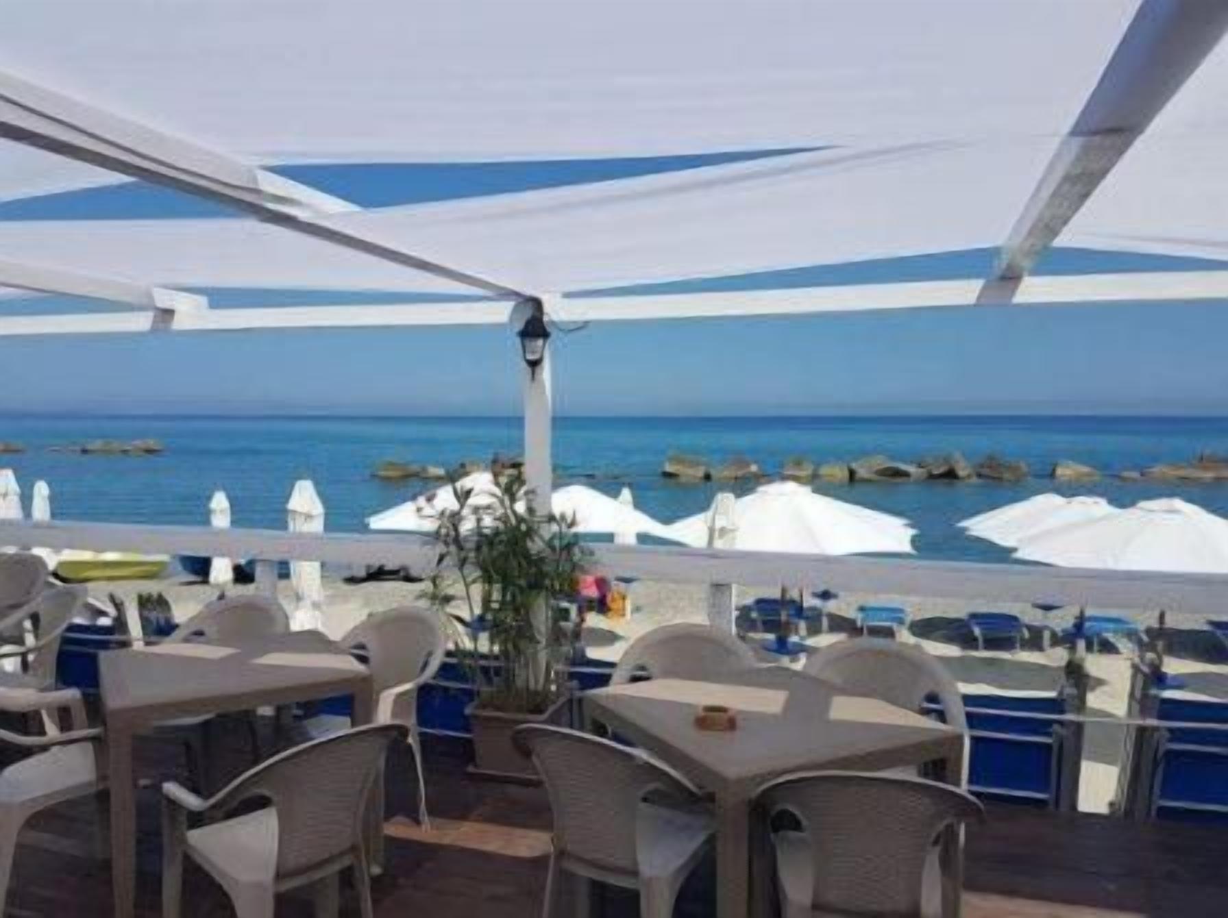 An outdoor dining area with tables and chairs, white umbrellas, and a view of the sea.
