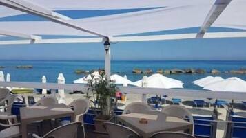 An outdoor dining area with tables and chairs, white umbrellas, and a view of the sea.