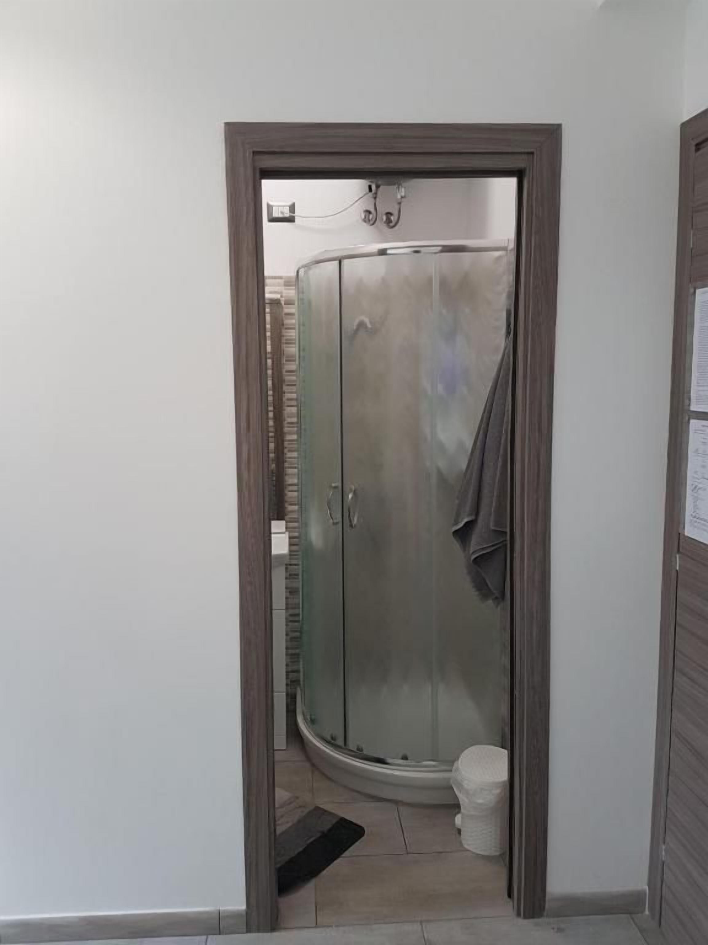 A bathroom with a glass shower enclosure, a toilet, and a door leading to another room.