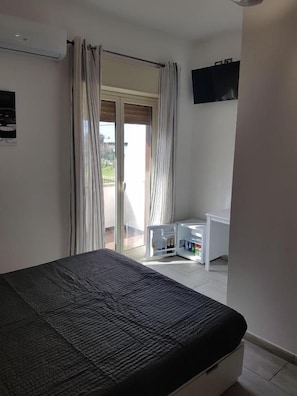Quarto com cama, escrivaninha e televisão na parede.
