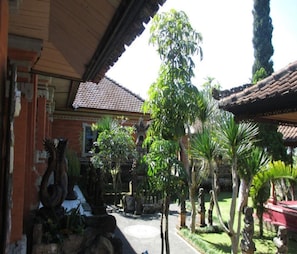 A courtyard with a tiled roof, stone statues, and lush greenery. - Cozzy The Dewata Homestay (Baturiti)