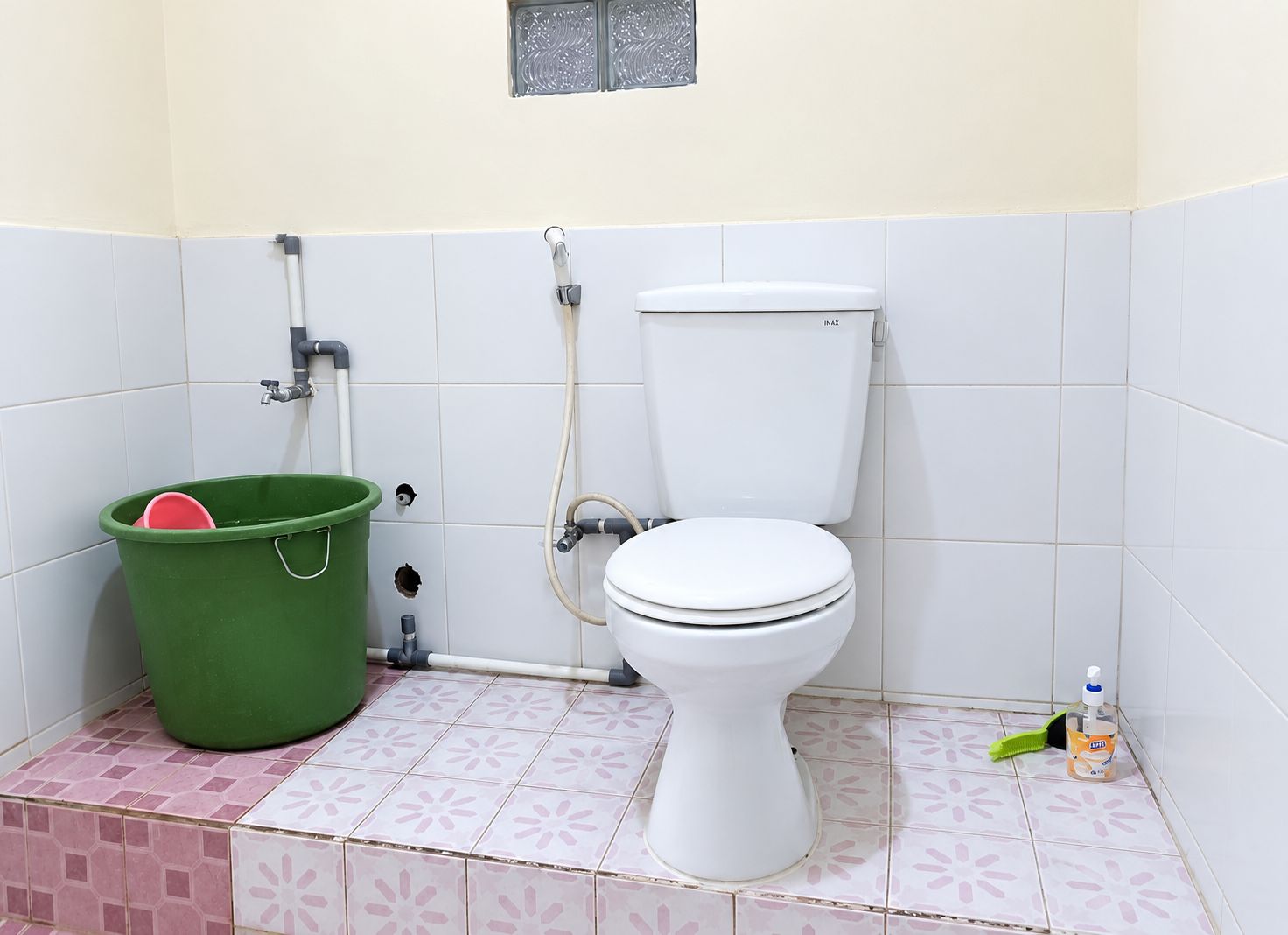 Un baño con un inodoro, un balde verde y un dispensador de jabón para manos.