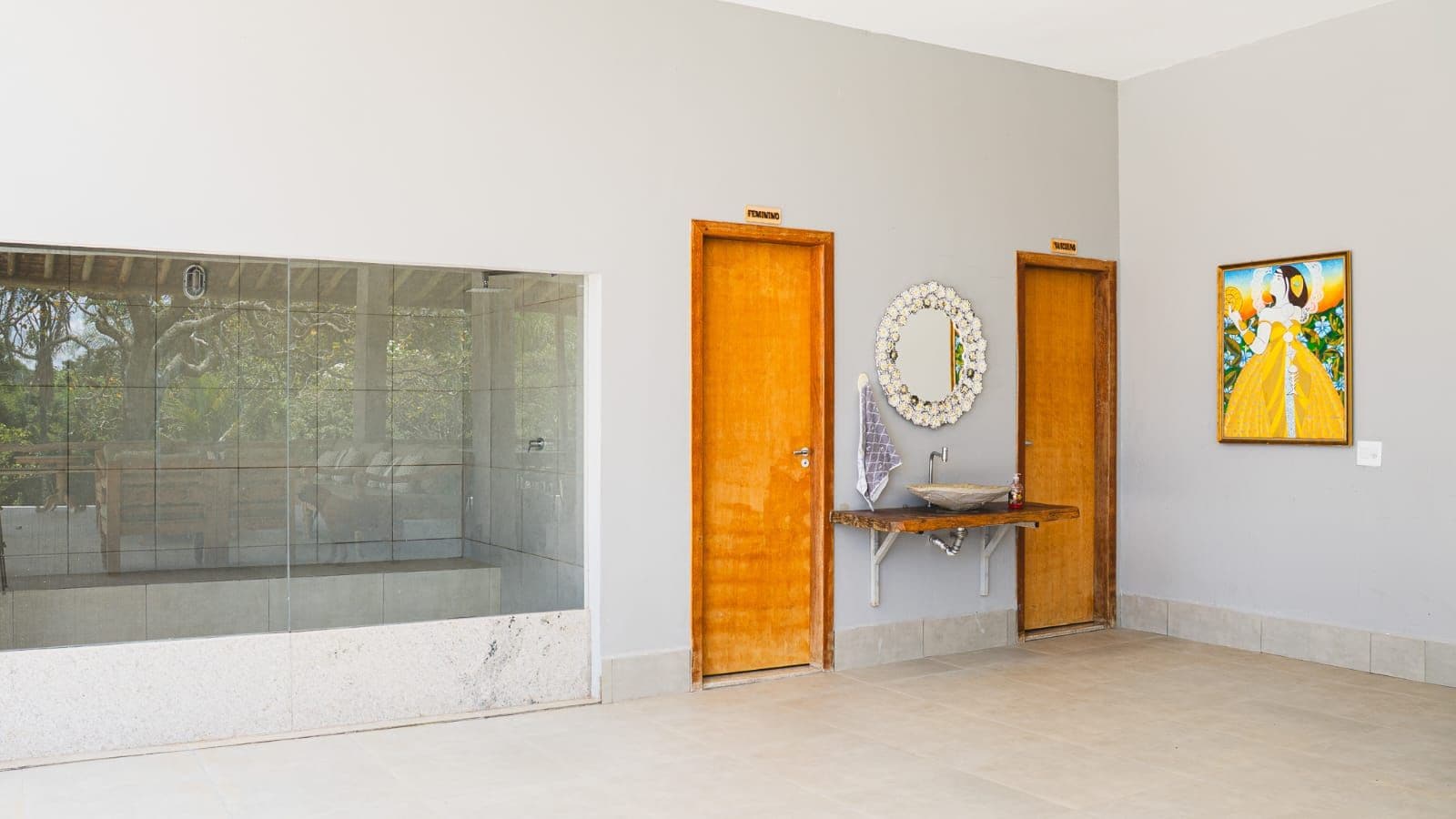 A room with a large glass window, wooden doors, a sink with a mirror, and a framed picture on the wall.
