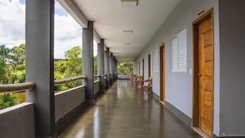 A corridor with a wooden railing, doors, and a view of greenery.
