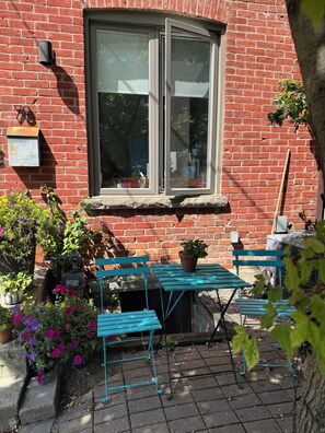 En byggnad av tegel med ett fönster, ett blått bord och krukväxter.