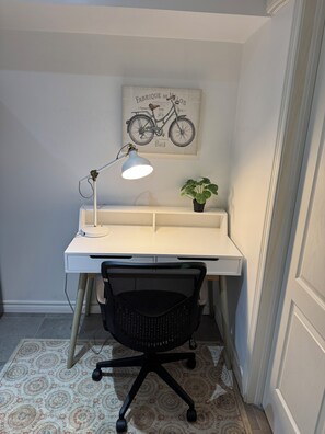 Een werkplek met een bureau, stoel, lamp en een fietsillustratie aan de muur.