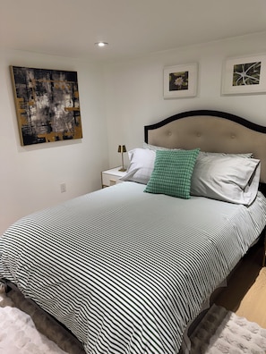 Una cama bien hecha con ropa de cama a rayas, una lámpara de noche y un cuadro colgado en la pared.