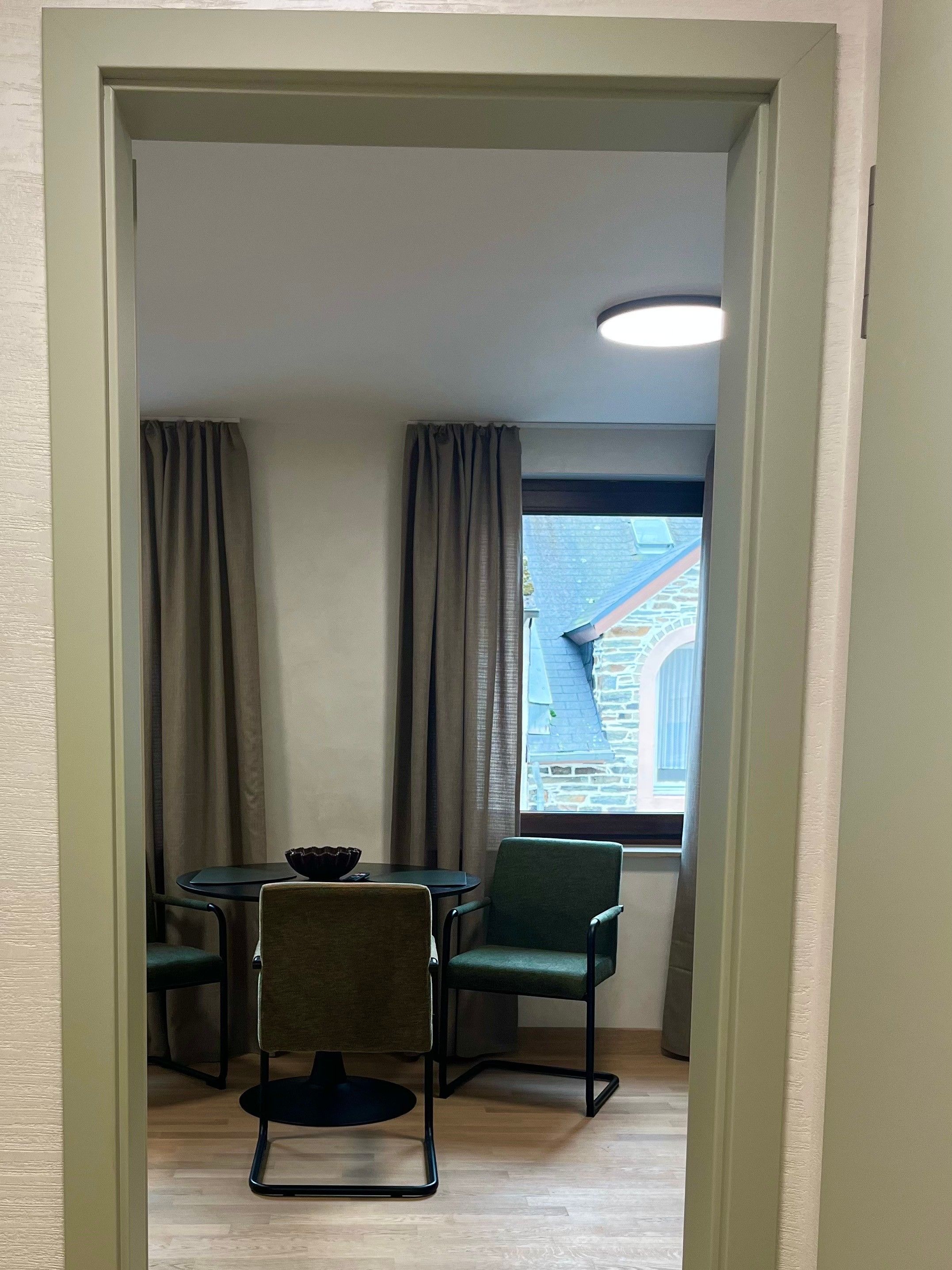 Ein Zimmer mit Esstisch und Stühlen, einem fenster mit Vorhängen und Blick auf ein Gebäude.