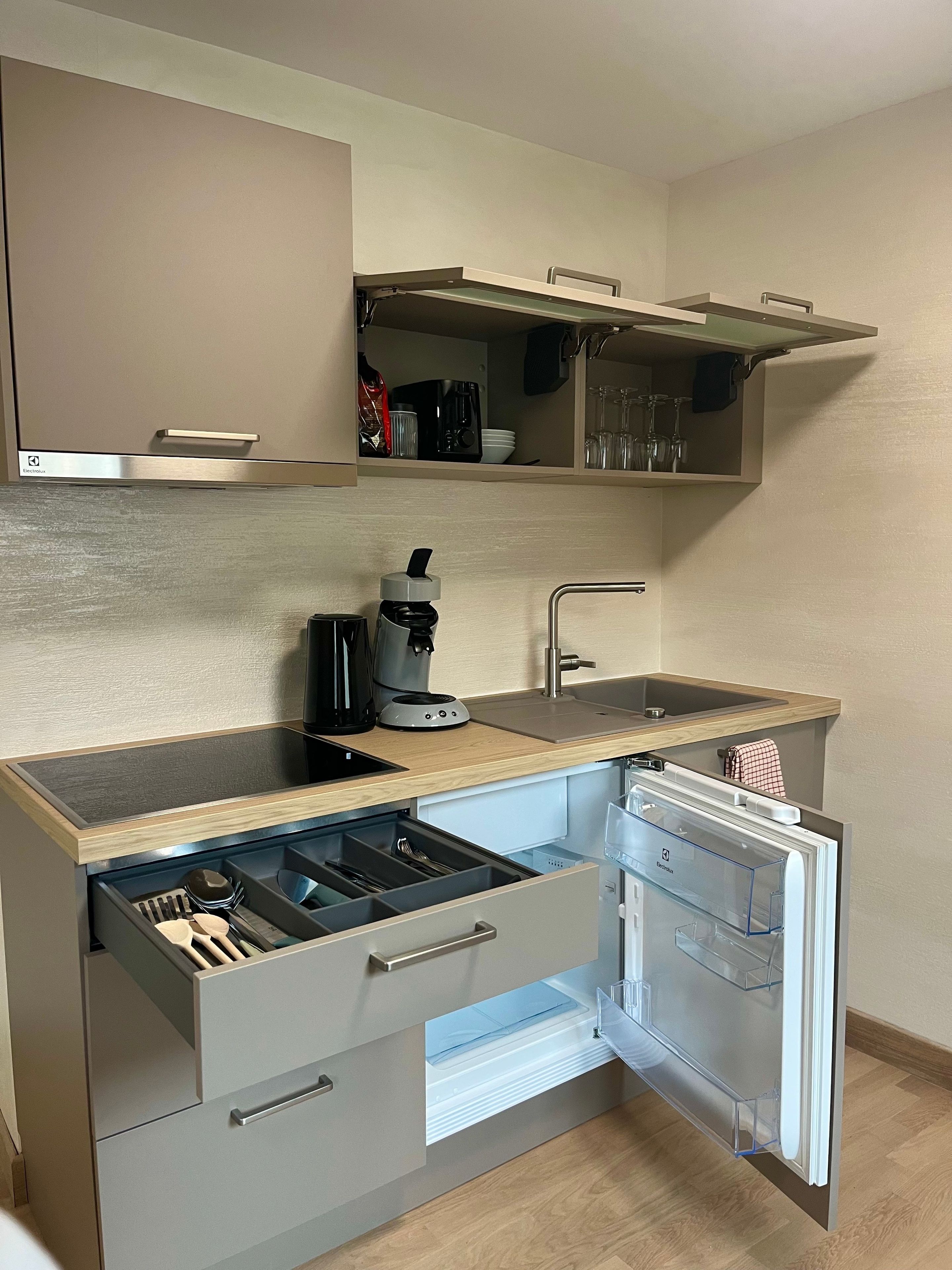 Une cuisine compacte équipée d’une machine à café intégrée, d’un lave-vaisselle et d’un petit plan de travail.