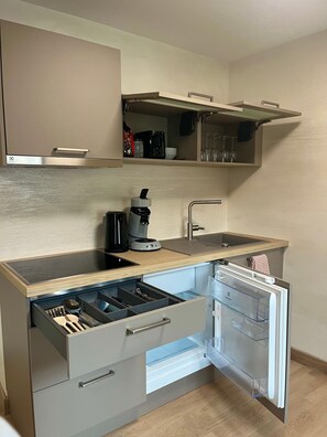 Une cuisine compacte équipée d’une machine à café intégrée, d’un lave-vaisselle et d’un petit plan de travail.