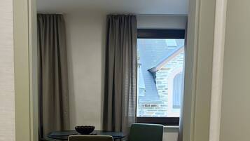 Ein Zimmer mit Esstisch und Stühlen, einem Fenster mit Blick auf ein Gebäude und einer Deckenleuchte.