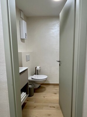 Ein kleines, schmales Badezimmer mit Toilette, Waschbecken und Mülleimer.