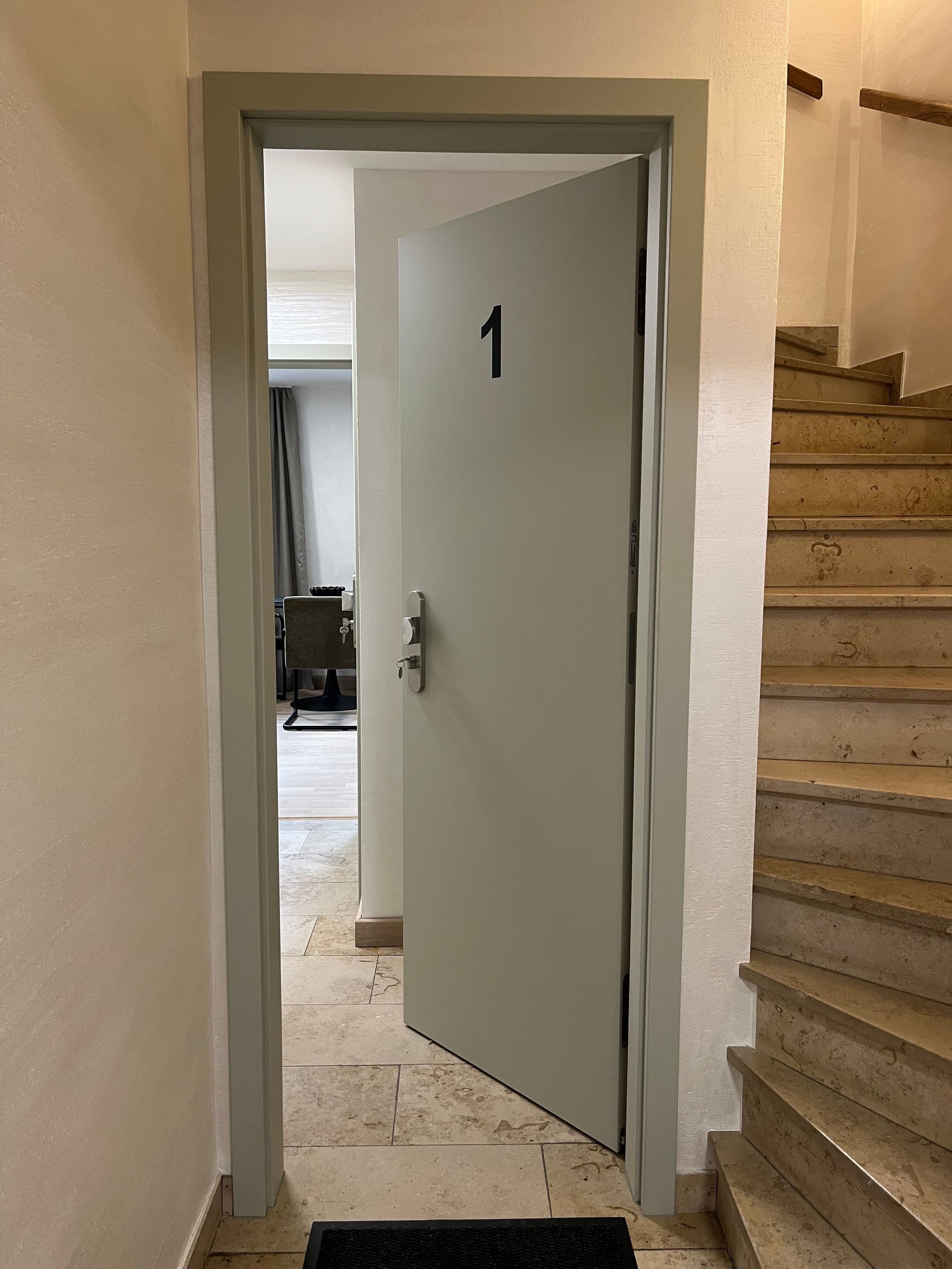 Un couloir mène à une porte portant le numéro 1, avec un escalier sur la droite.