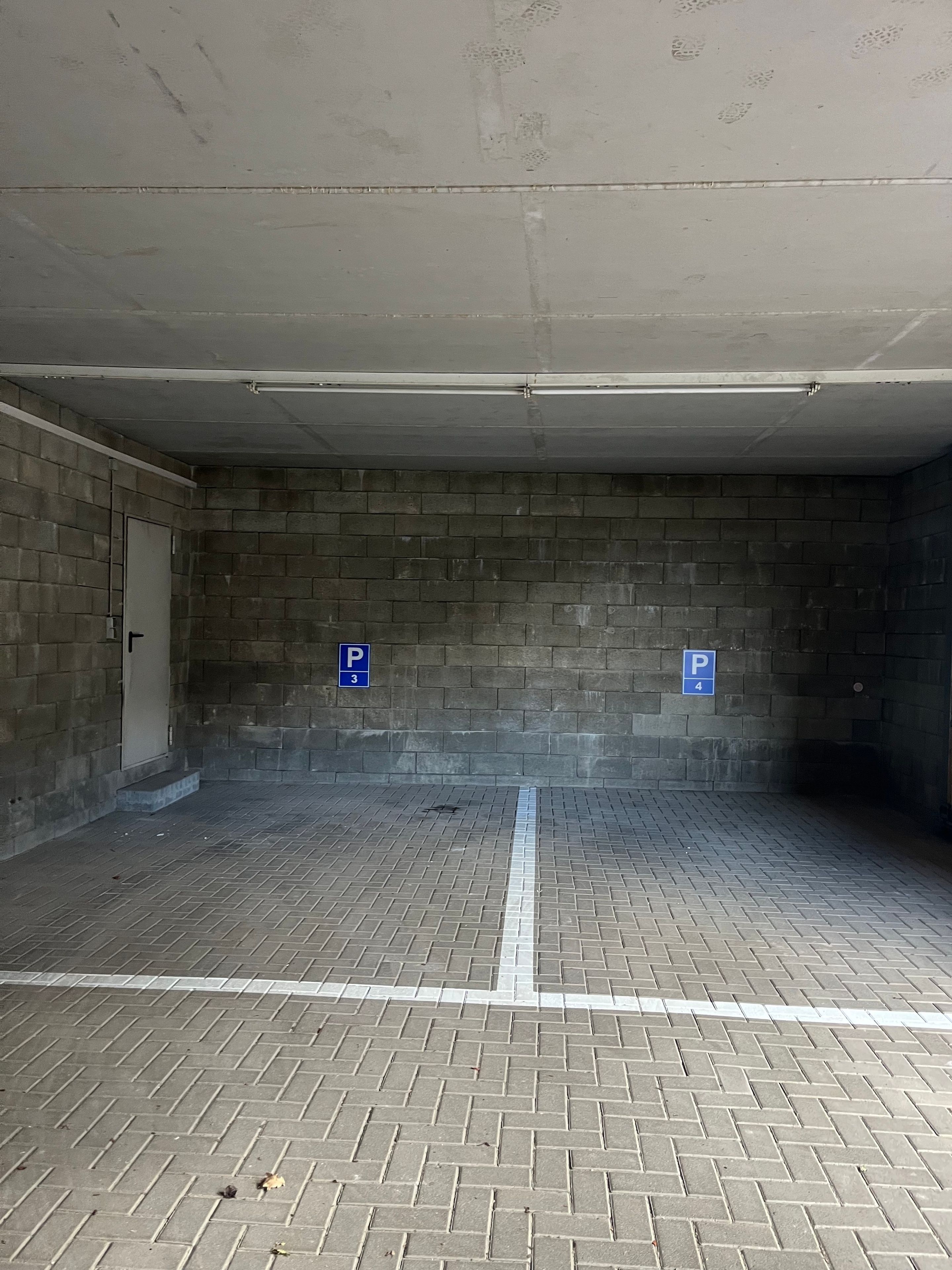 Eine Parkgarage mit Ziegelwänden und Fliesenboden, mit Parkplätzen, die mit den Nummern 3 und 4 gekennzeichnet sind.
