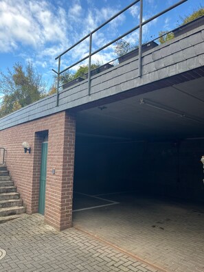 Et overdækket parkeringsområde med murstensvæg, grøn dør og gelænder på en viadukt.