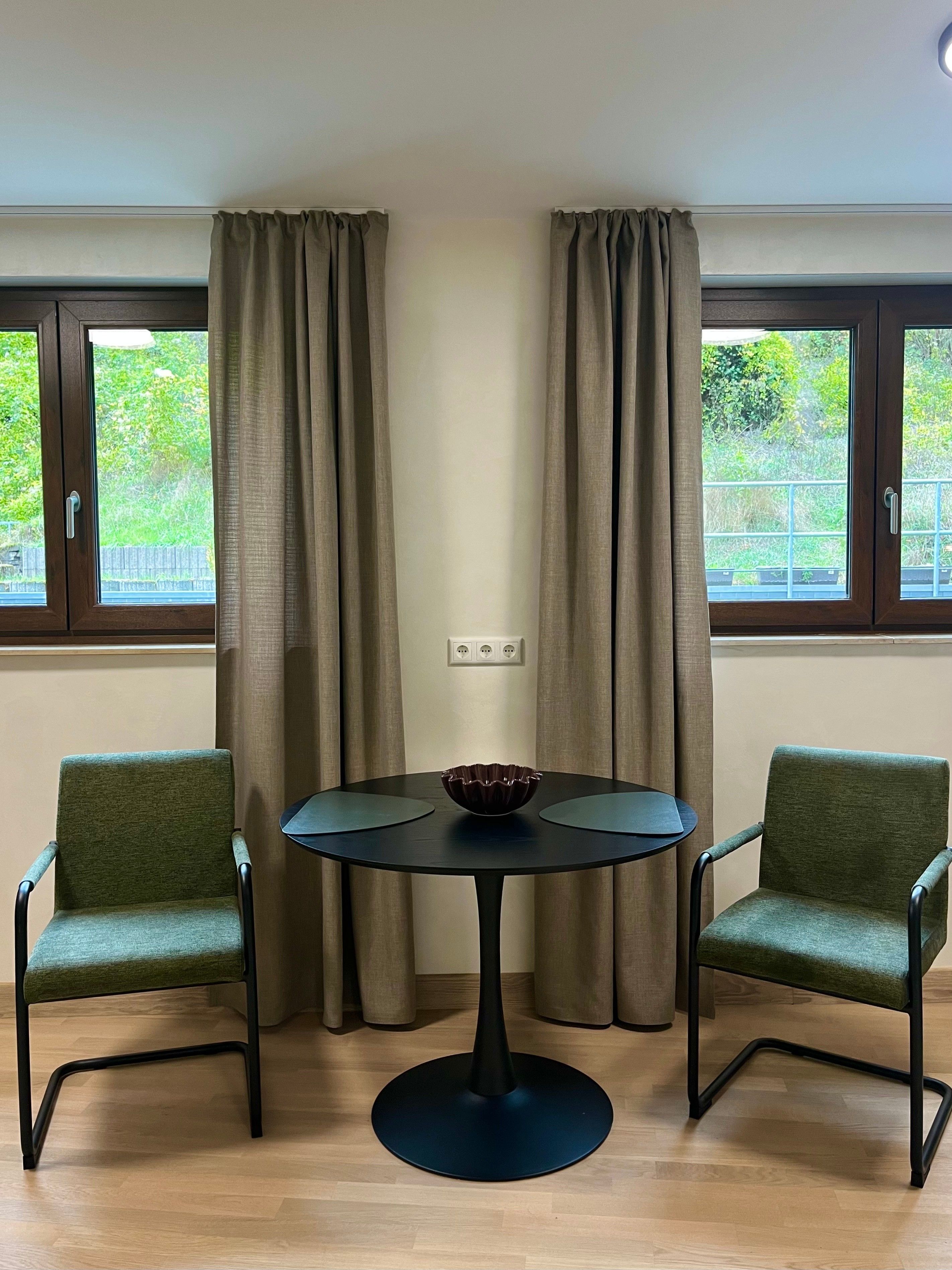 Ein Zimmer mit einem runden Tisch, zwei Stühlen und einem Fenster mit Vorhängen.