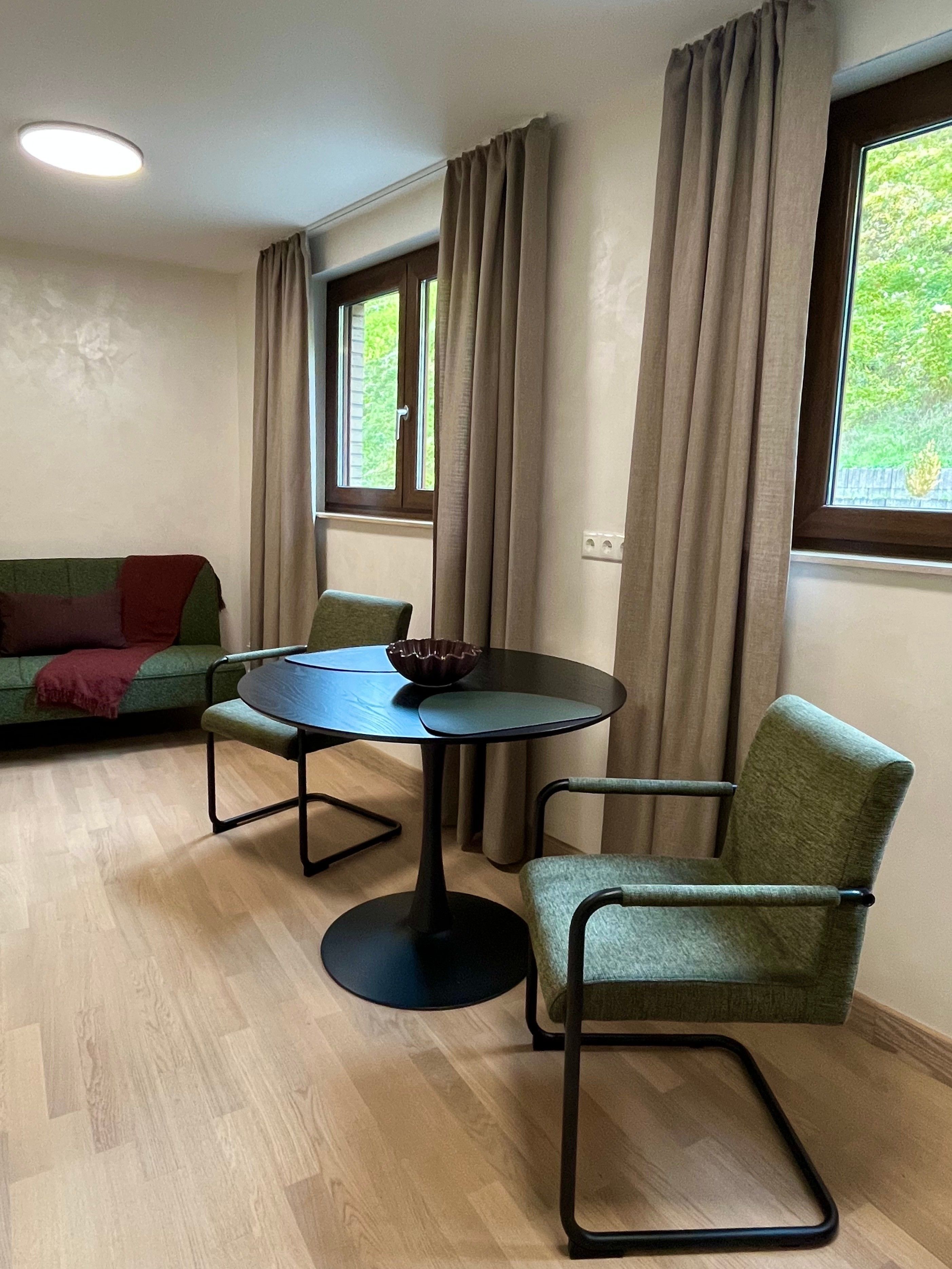 Una habitación con una mesa redonda, dos sillas, un sofá y una ventana con cortinas.