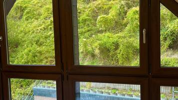 Ein Zimmer mit großen Fenstern, einem Bett und Blick auf eine Ziegelwand und Grünflächen.