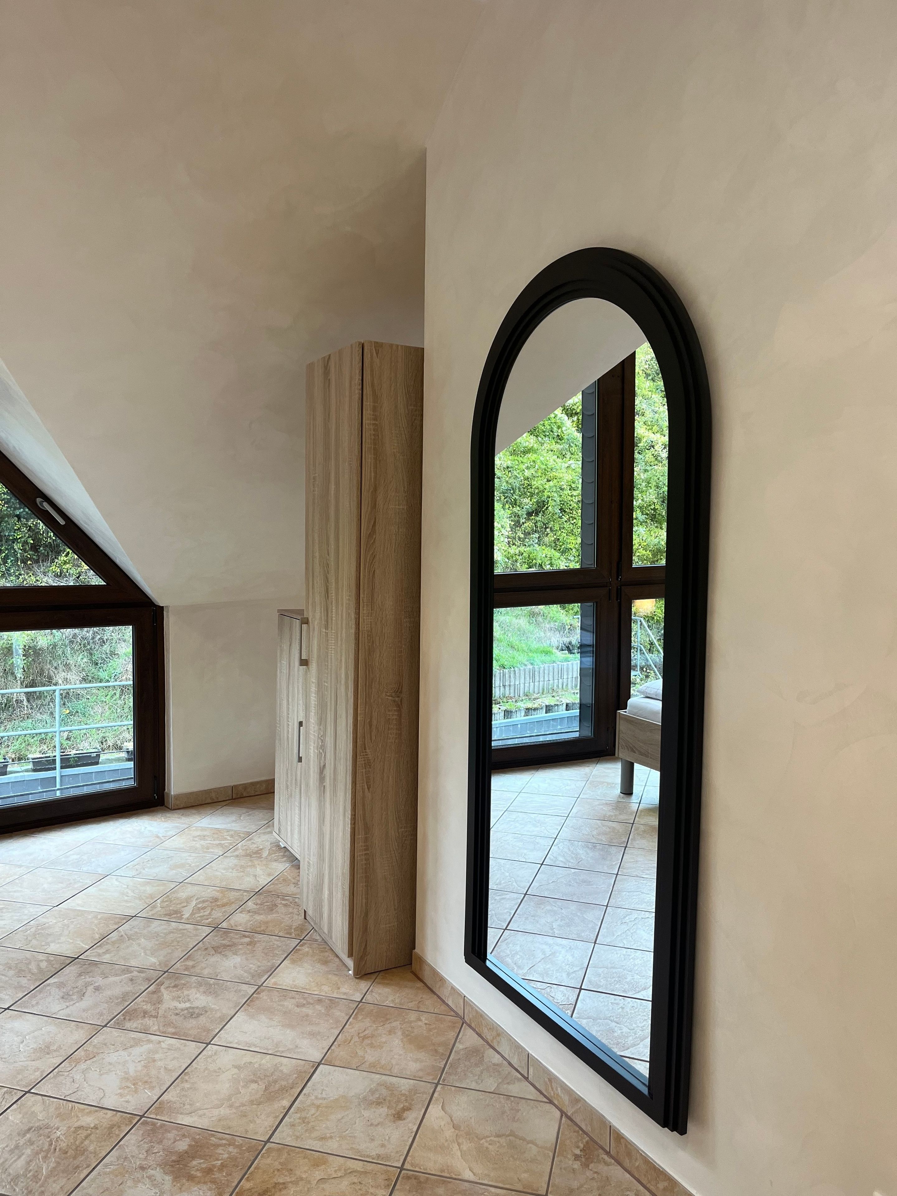 A spacious room with large windows, a wooden cabinet, and a tiled floor.