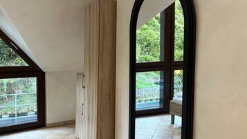 A spacious room with large windows, a wooden cabinet, and a tiled floor.