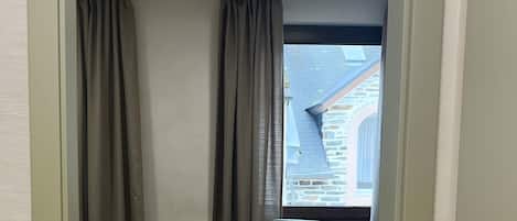 A room with a dining table and chairs, a window with a view of a building, and a ceiling light.