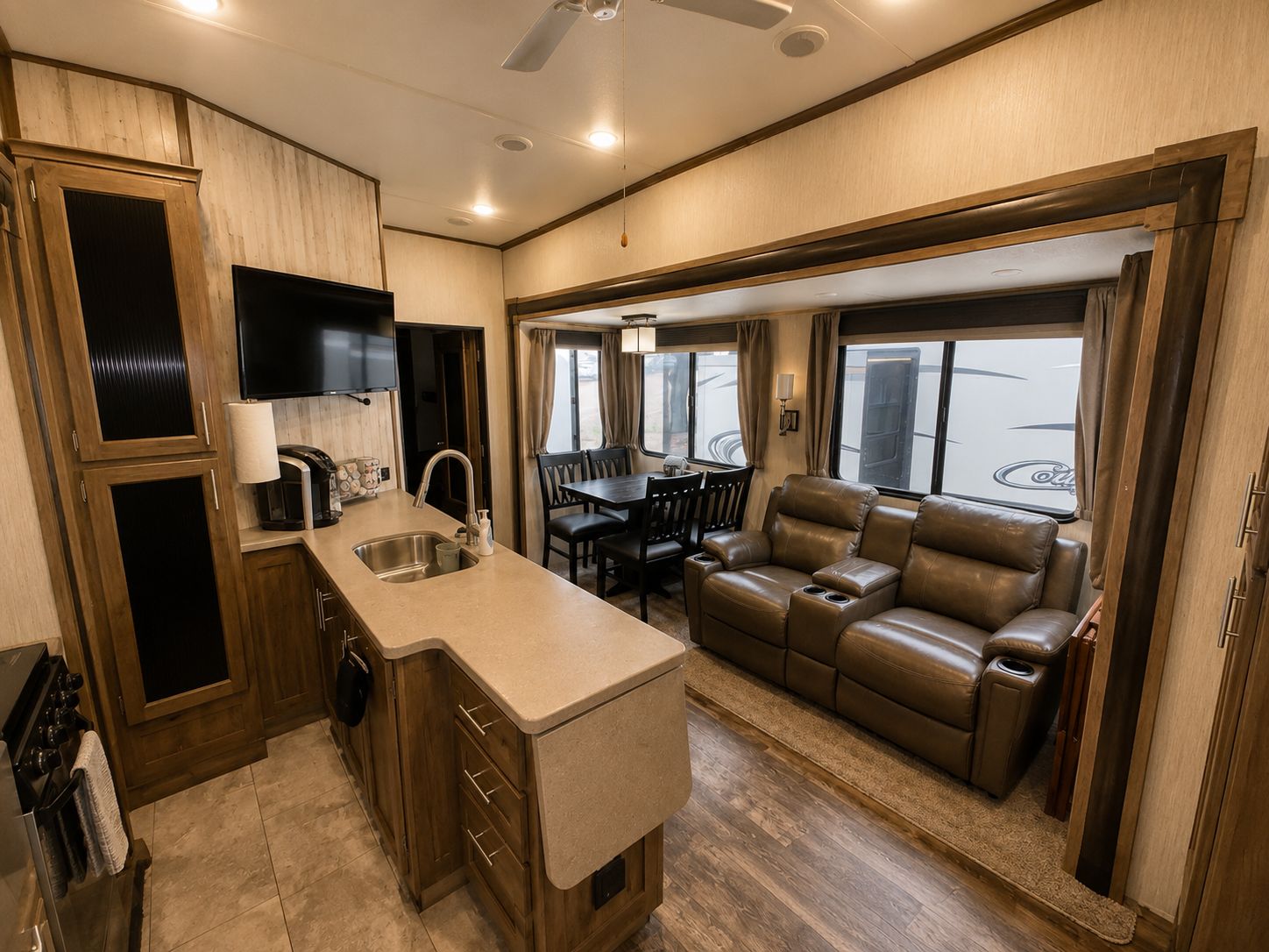 A compact RV kitchen with a sink, stove, and a flat-screen TV.
