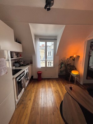 Cocina compacta con lavadora, una pequeña mesa de comedor y ventana con vistas a edificios.