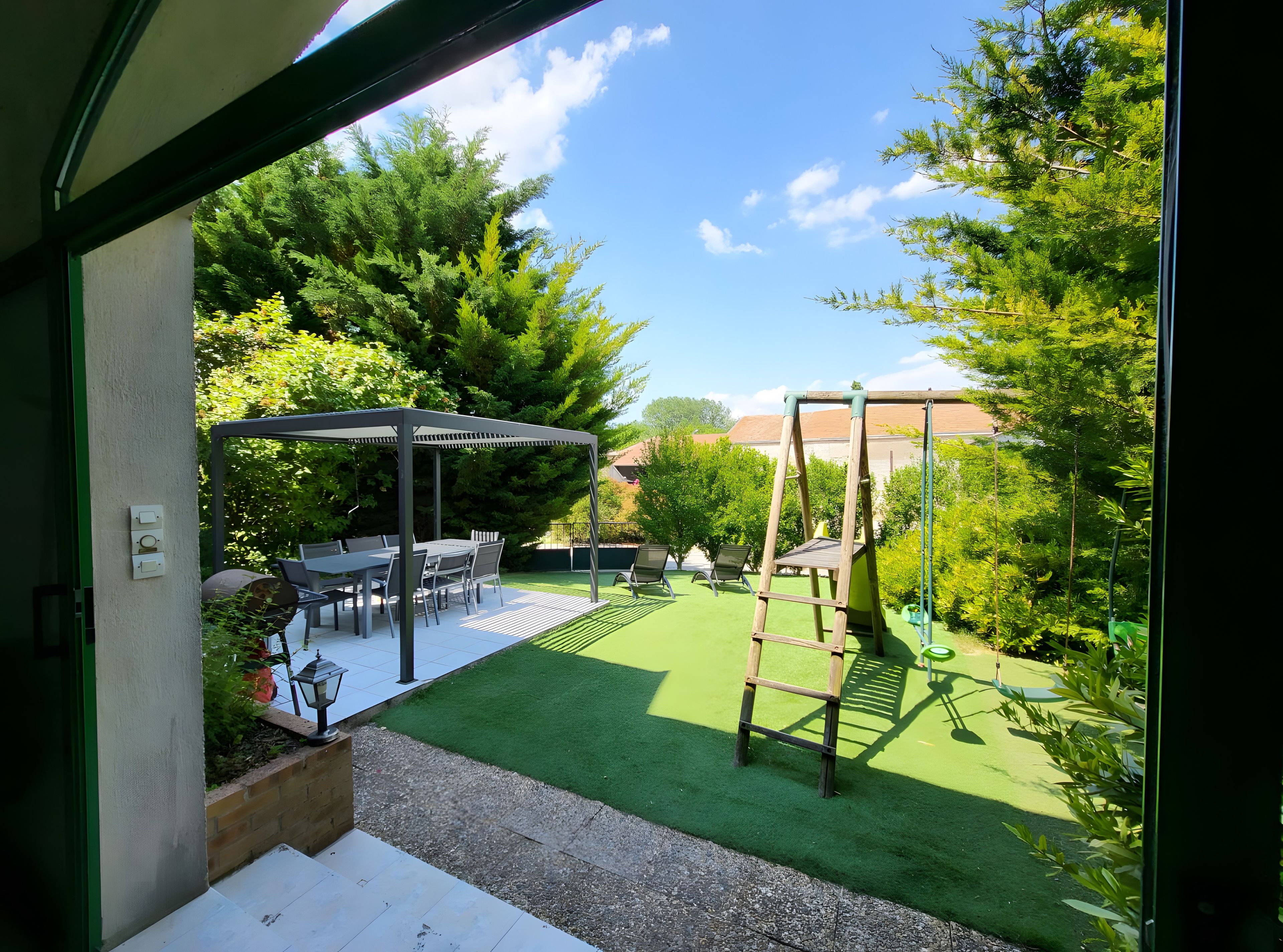 A patio with a table and chairs, a swing set, and a pergola.