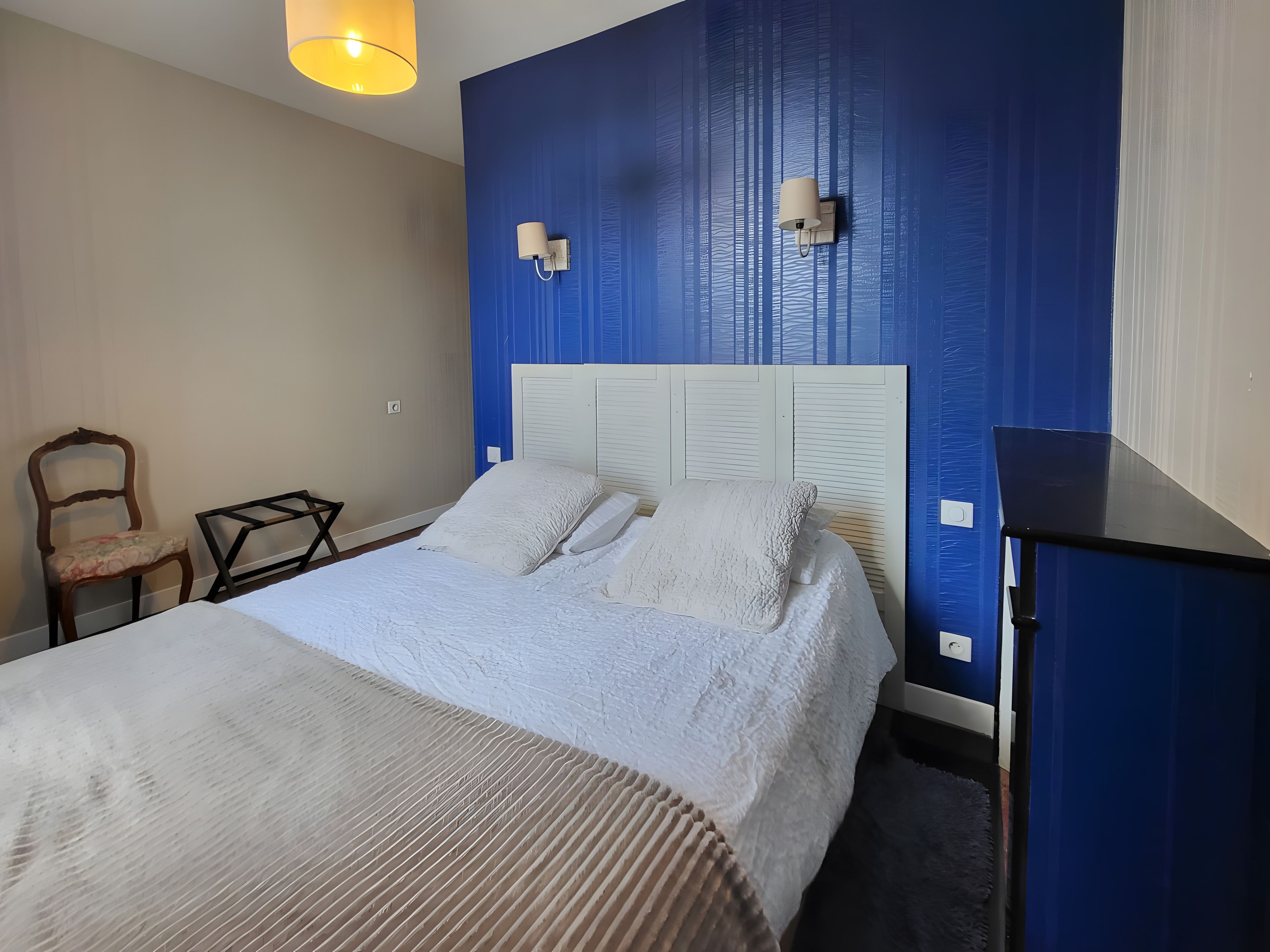 Une chambre à coucher comprenant un lit, une chaise, une table de chevet et une lampe fixée au mur.