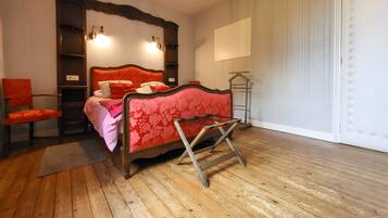 A bedroom with a wooden floor, a bed with a red headboard, a chair, and a bedside table.