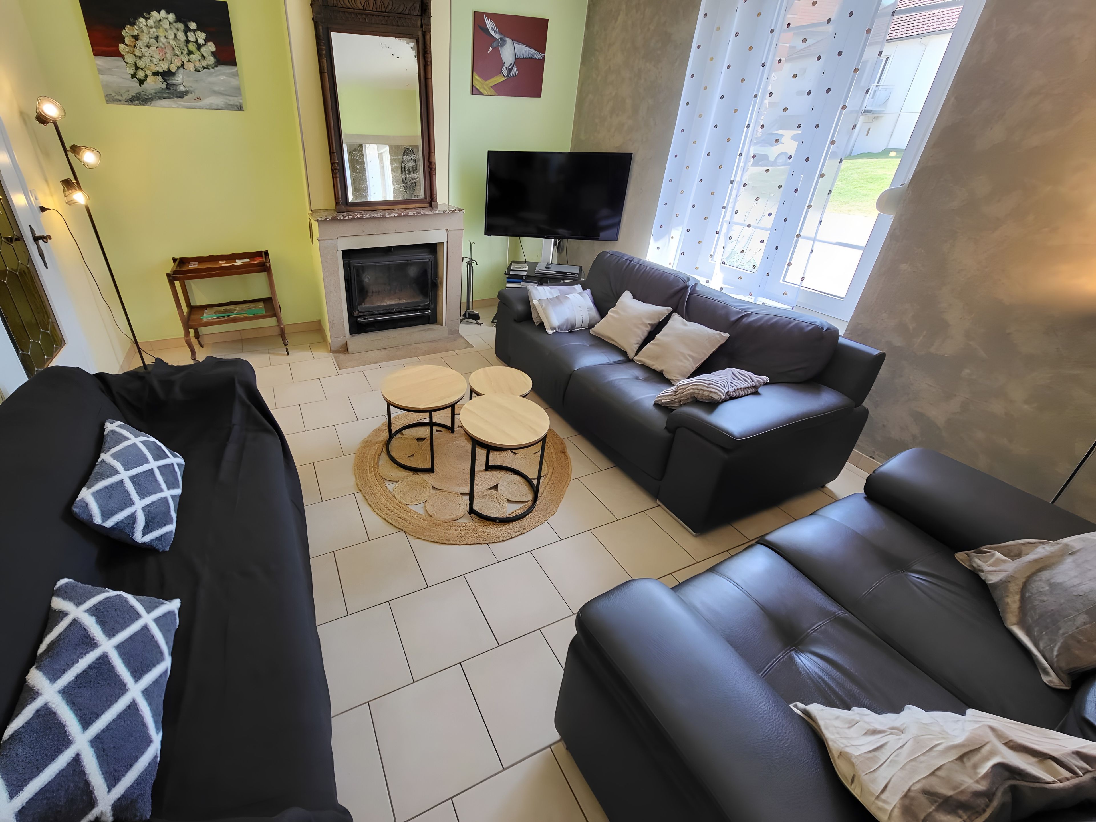 A living room with a fireplace, two sofas, a TV, and a large window.