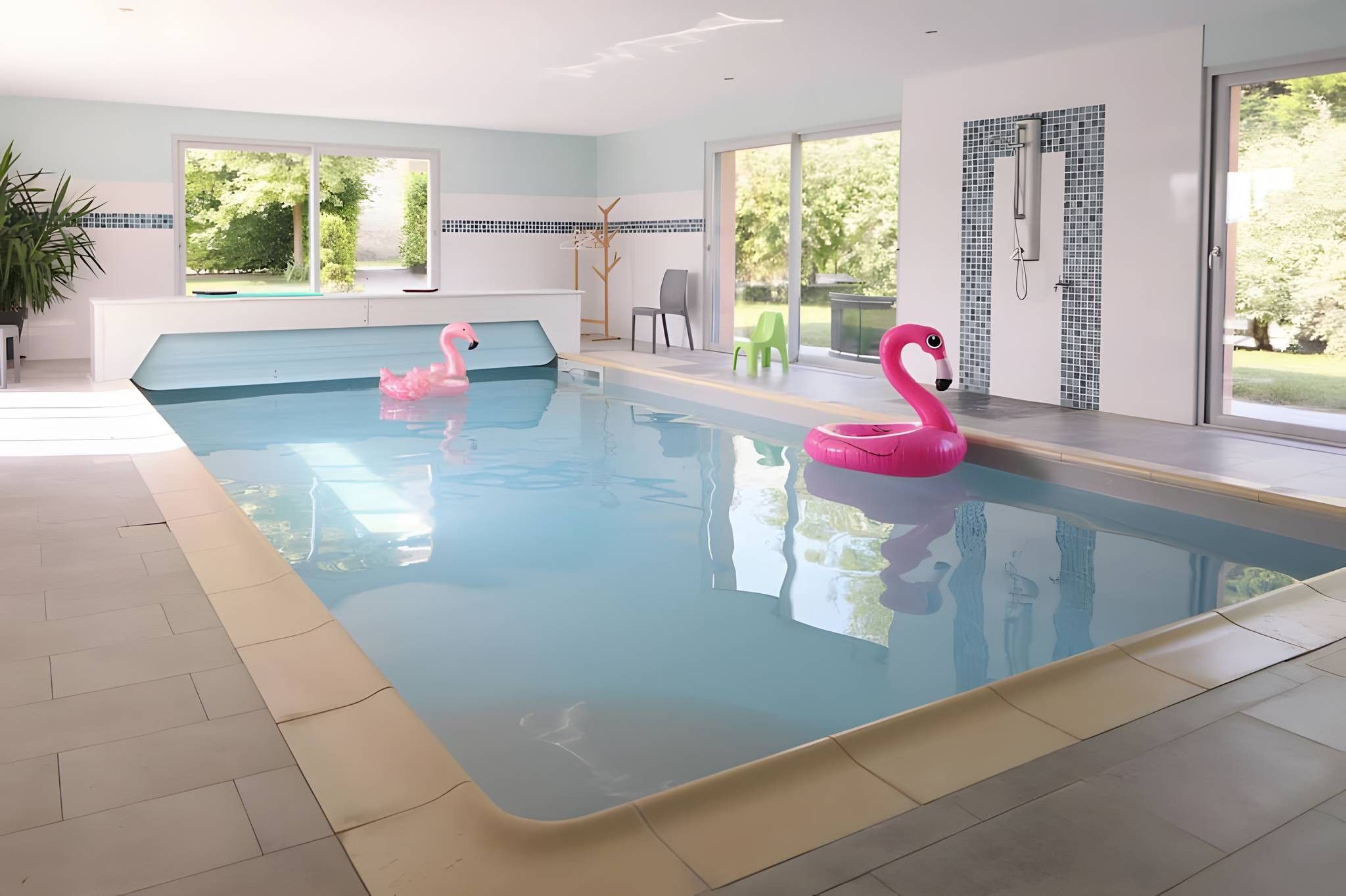 A swimming pool with two pink flamingo floats, a potted plant, and a view of greenery outside.