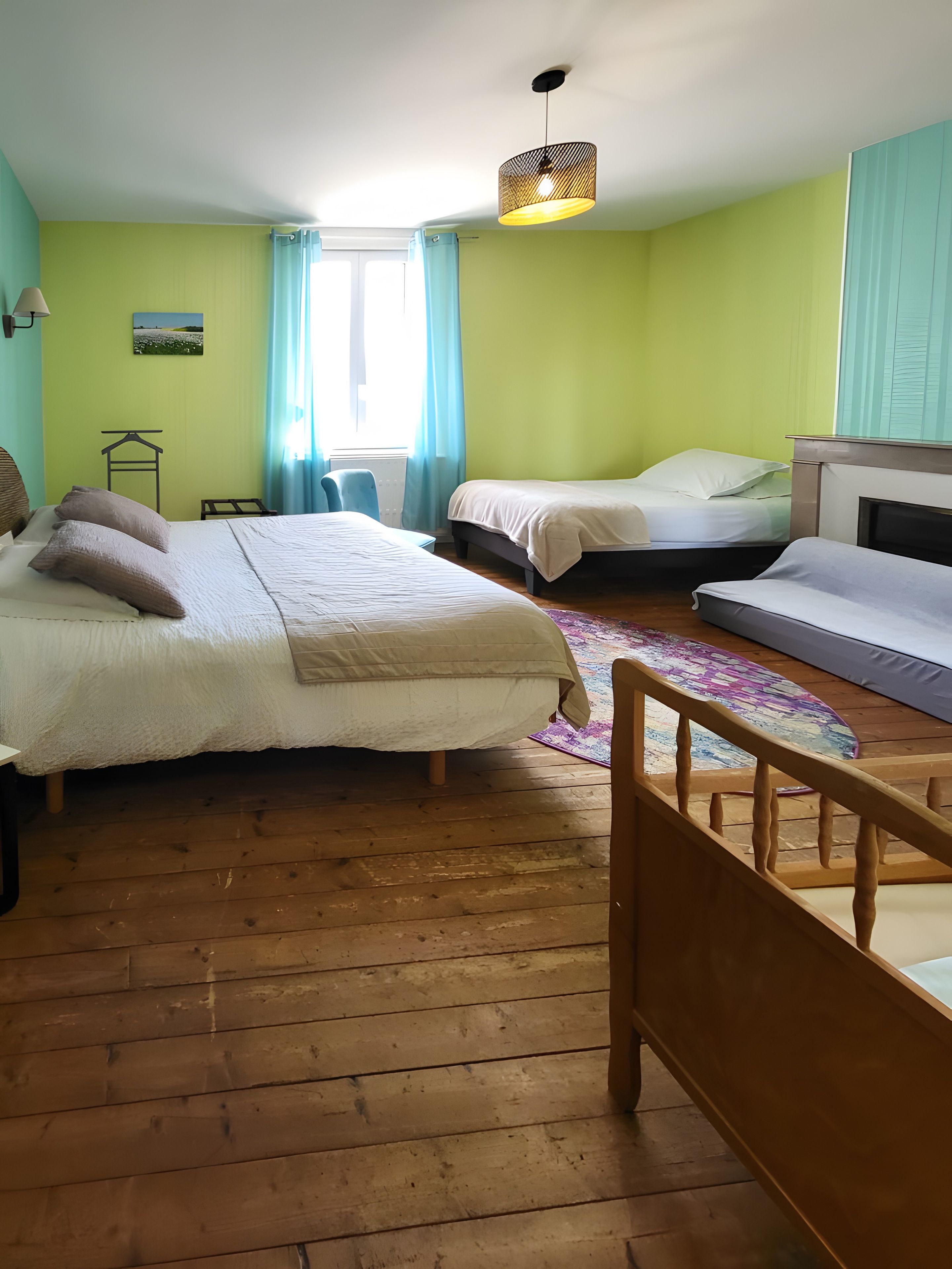 Une chambre avec deux lits, un plancher en bois, un luminaire suspendu et une fenêtre avec des rideaux.