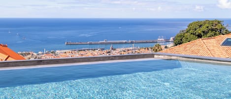 Piscina azul e límpida com vista para o mar e um cais distante.
