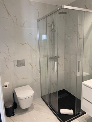 Moderni kylpyhuone, jossa on lasiseinällä varustettu suihku, wc ja roskakori.