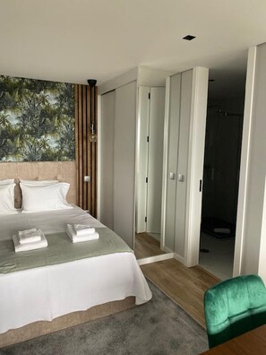 Hotellihuone, jossa on sänky, vihreä tuoli, vaatekaappi ja ovi, joka johtaa kylpyhuoneeseen.
