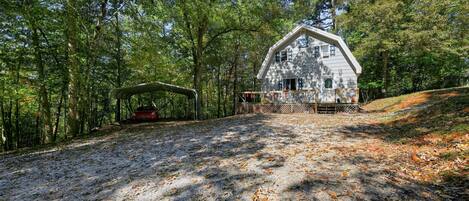 A rustic cabin with a covered porch, surrounded by a forested area.