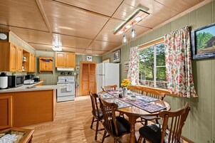 Una cocina con armarios de madera, una mesa de comedor con sillas, un refrigerador y una ventana con cortinas florales.